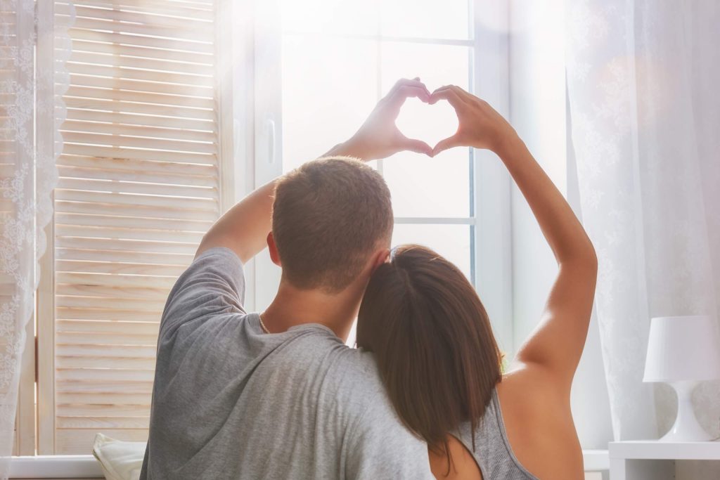 A couple in a bedroom making a heart shape with their hands, illustrating their love and connection in marriage.