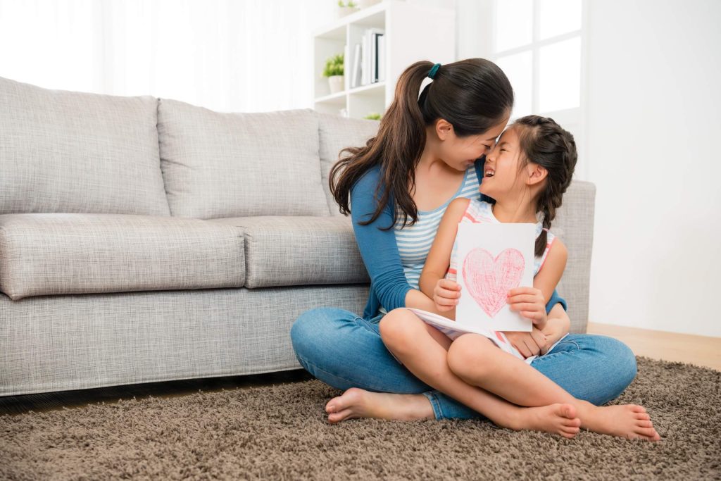 A woman and her daughter sit on the floor, surrounded by a large heart, representing love.