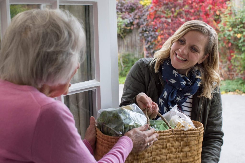 A woman presents a basket of food to an older woman, illustrating a heartfelt gesture of love.