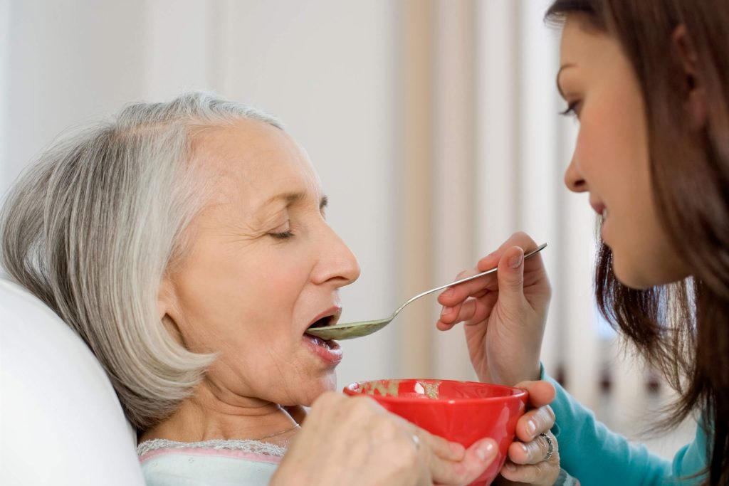 A caring woman gently feeds an elderly woman soup, highlighting a tender moment of love.