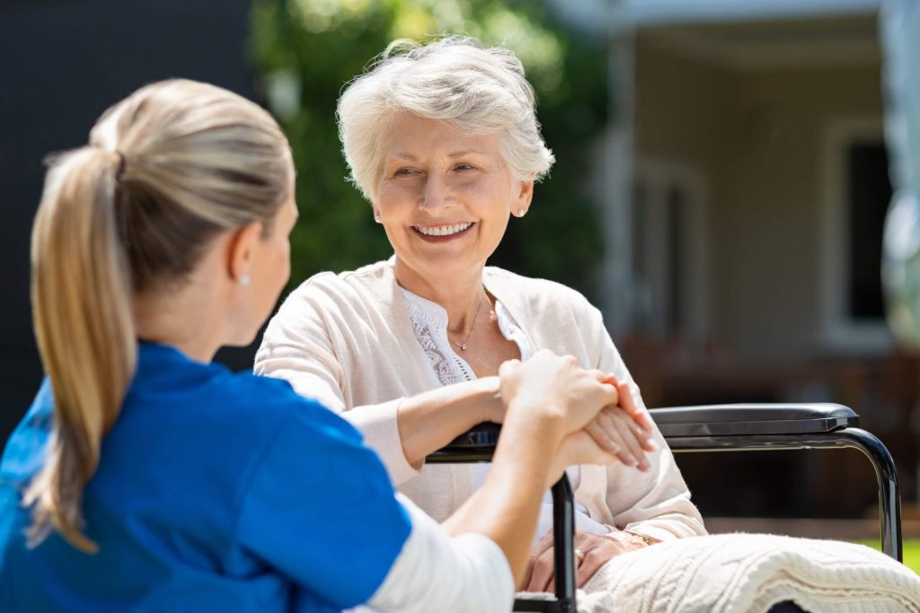 An elderly woman in a wheelchair converses with a nurse, representing love for the sick in need of care.