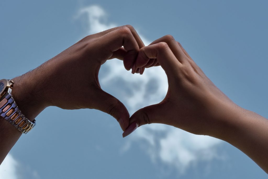 A heart shape created by hands with a clear blue sky in the background, representing, love in celebration of Valentine's Day.
