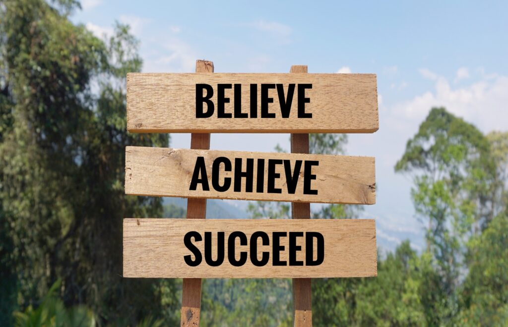 A rustic wooden sign featuring the phrases "believe, achieve, succeed," representing inspiration for graduation and future goals.